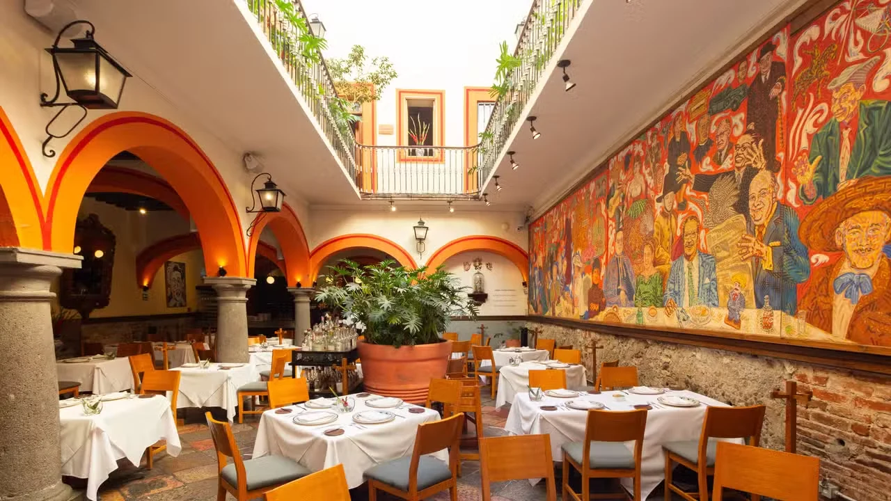 Patio de El Mural de los Poblanos, con arcos naranjas y el gran mural junto a las mesas